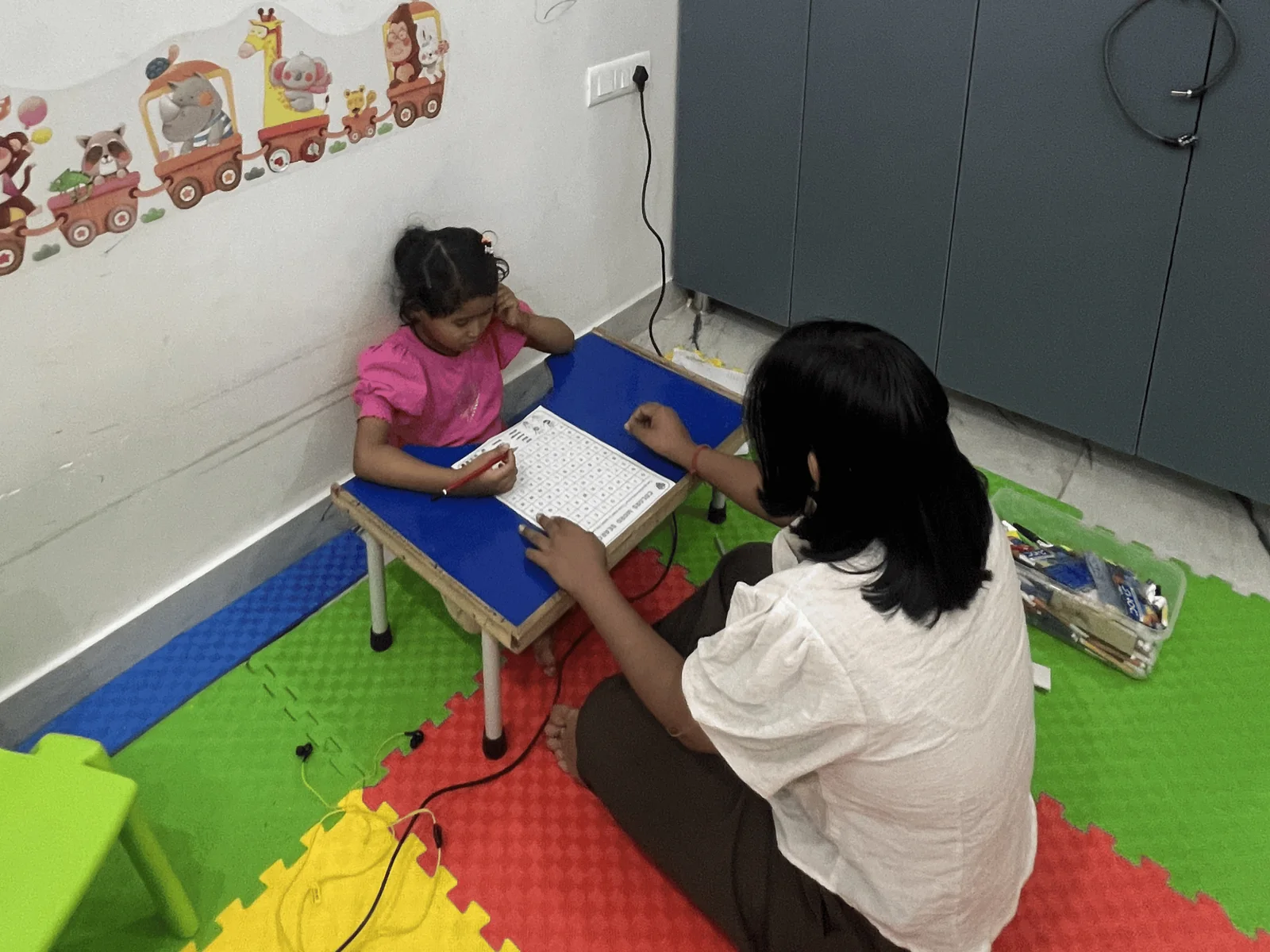 A child working through a worksheet at a low table with a therapist sitting alongside
